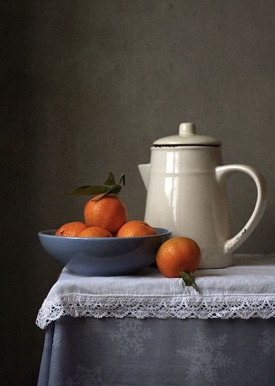 a bowl of oranges sitting on top of a table next to a tea pot