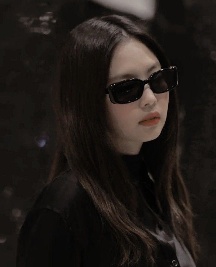 a woman with long hair wearing sunglasses and looking off to the side while standing in front of a black background