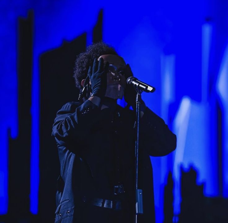 a man standing in front of a microphone holding his hand up to his face while wearing a black jacket