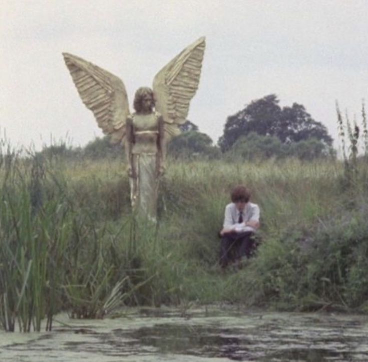 a man sitting in the grass next to a statue with an angel on it's back