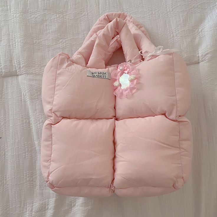 a pink handbag with a flower on the front and side pocket is laying on a bed