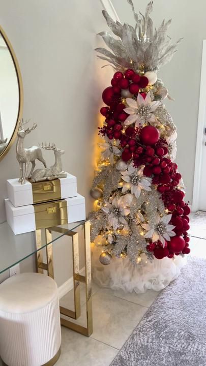 a white christmas tree with red and silver decorations next to a mirror on the wall