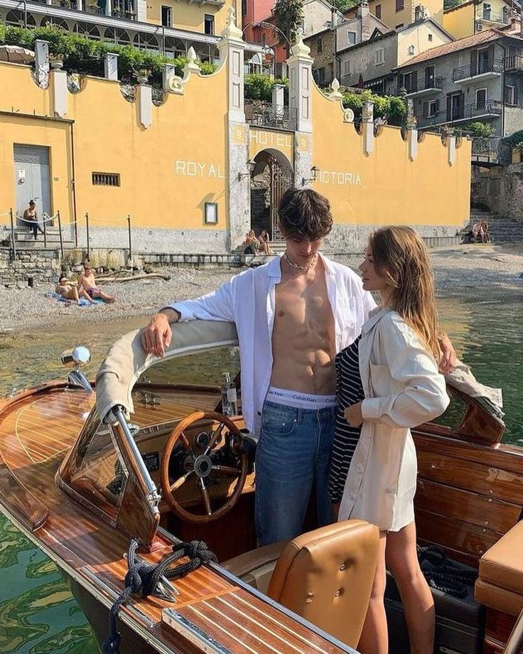 a man and woman standing on the deck of a small boat in front of a yellow building