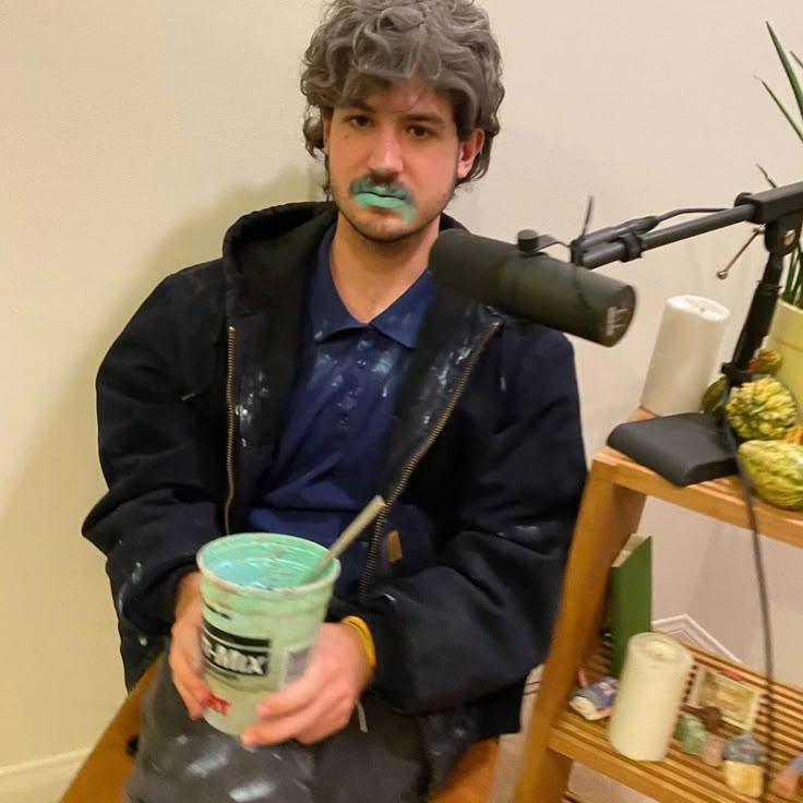 a man sitting on a chair holding a green cup with something painted on his face