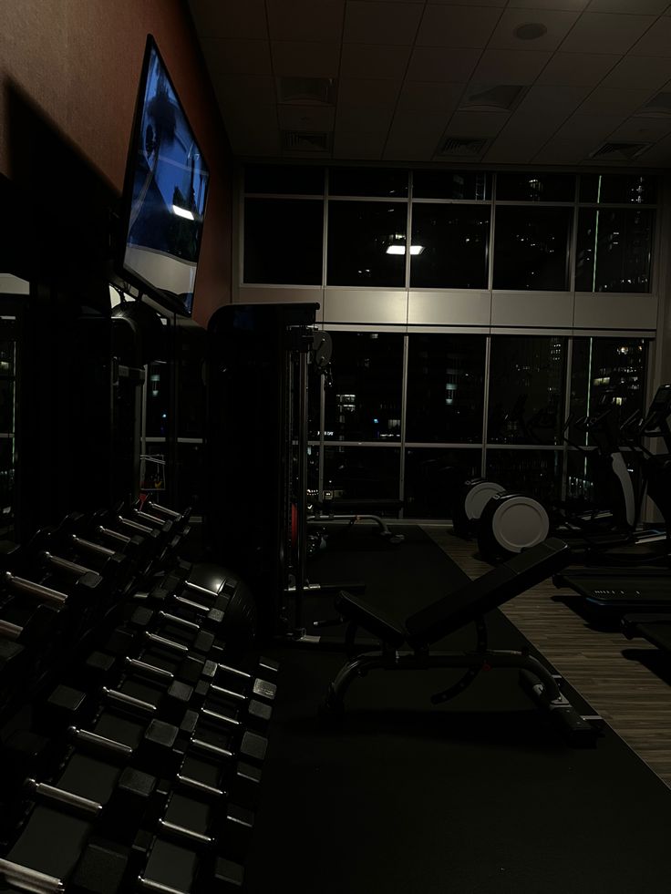 there is a television and treadmills in the dark room with no one on it