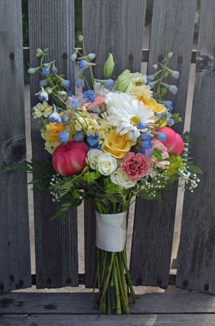 a bouquet of colorful flowers sitting on top of a wooden bench next to a fence