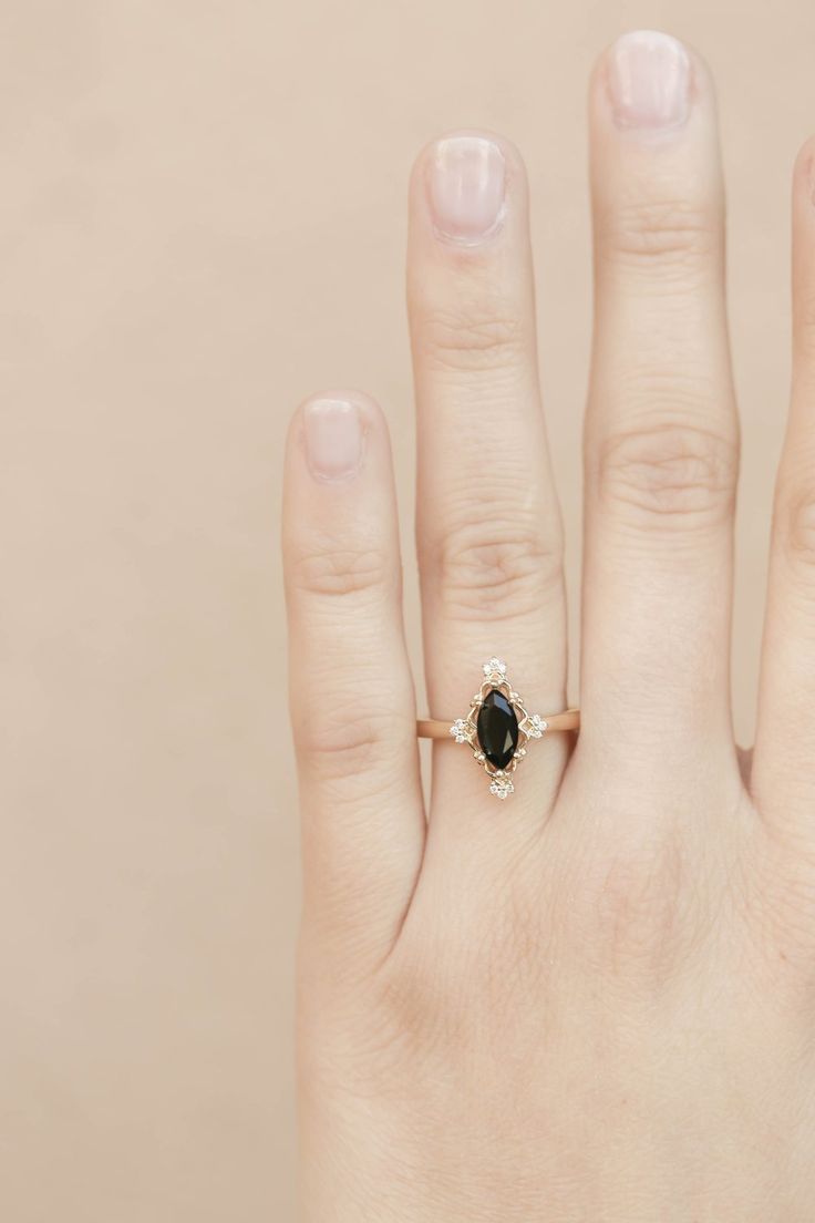 a woman's hand with a black diamond ring on her left hand, and a gold band around the middle finger