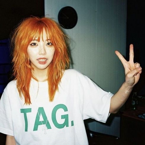 a woman with red hair and bangs making the peace sign while wearing a tag t - shirt