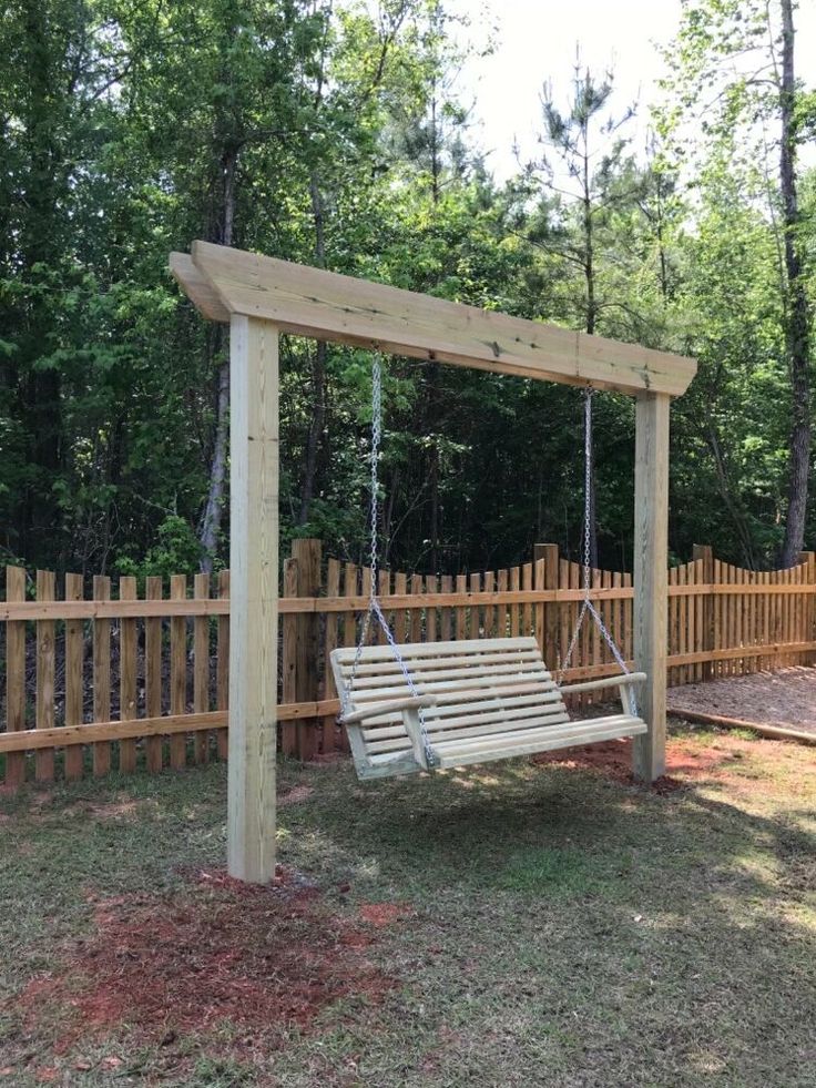 a wooden swing in the middle of a yard with a fence and trees behind it