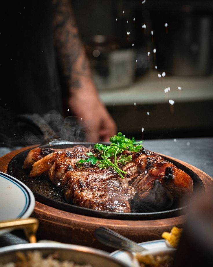 a plate with meat and vegetables on it in a restaurant kitchen, being sprinkled with seasoning