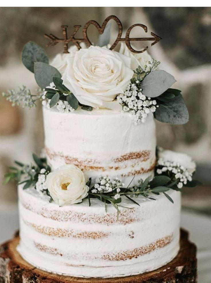 a wedding cake with white flowers and greenery on top sits on a wooden stand