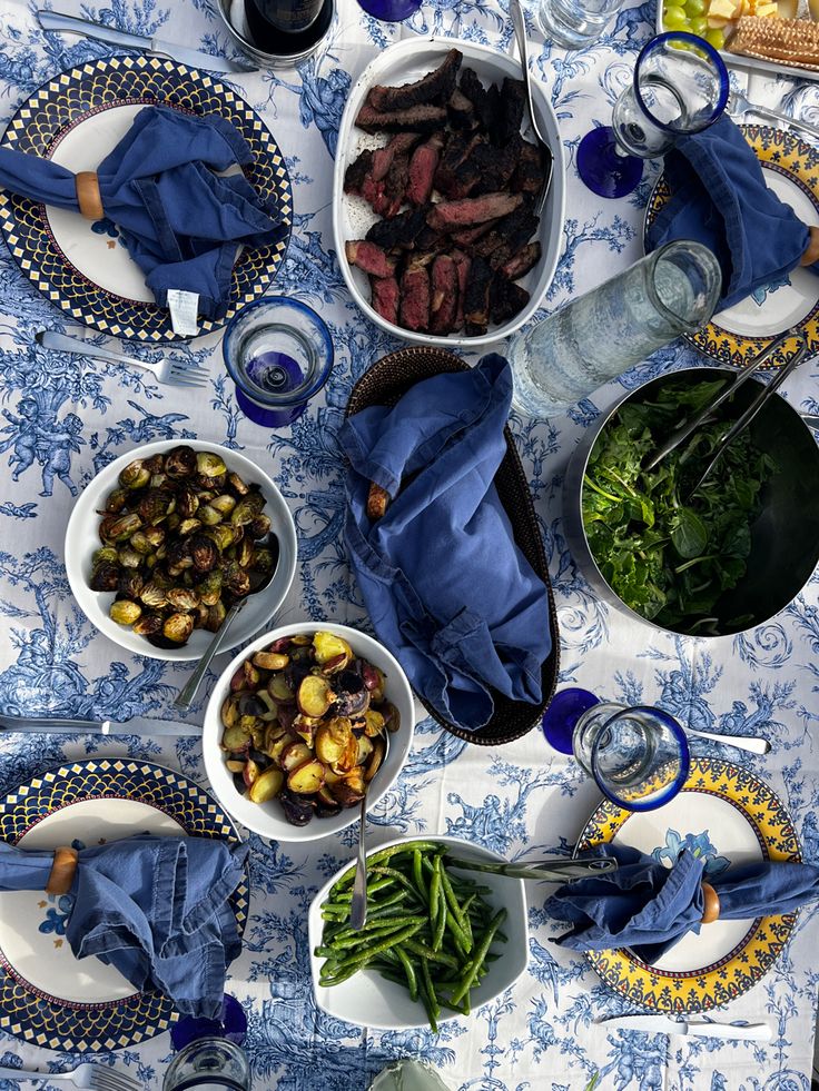 a table topped with plates and bowls filled with food next to wine glasses on top of a table cloth