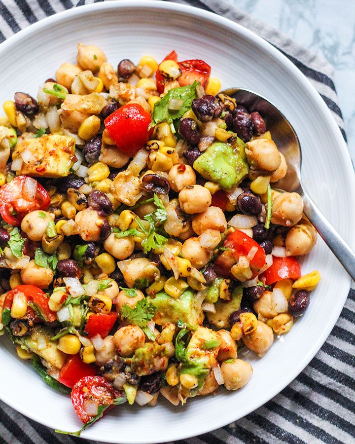 a white bowl filled with black beans, corn and avocado on top of a striped table cloth