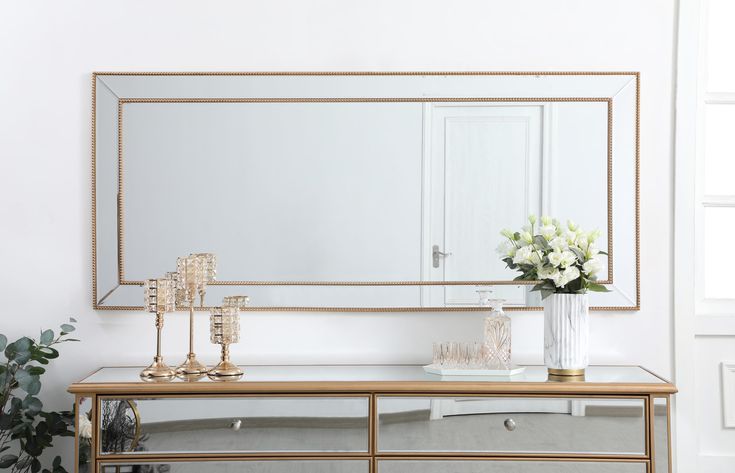 a large mirror sitting on top of a table next to a vase filled with flowers