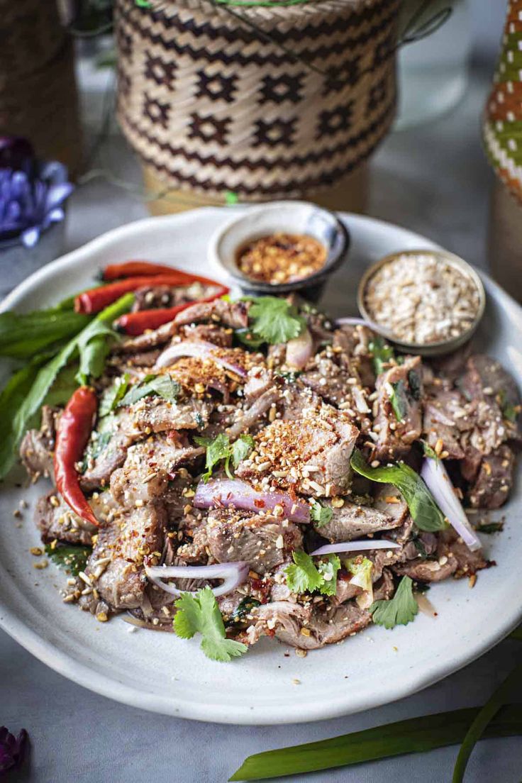 a white plate topped with meat and veggies next to bowls of seasoning