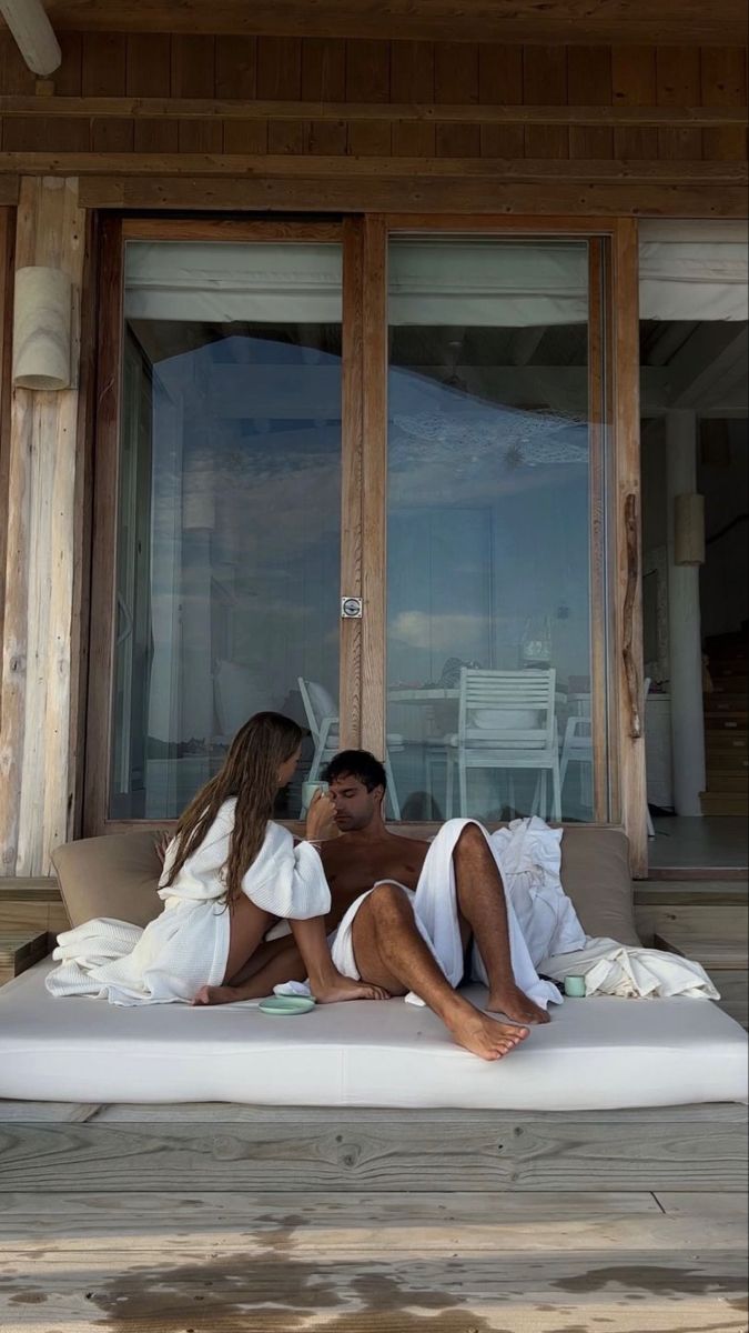 a man and woman are laying on a bed in front of an open glass door