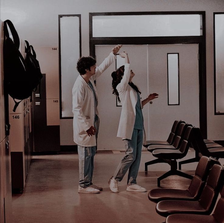 two people standing next to each other in an empty room with chairs and one person reaching up for something