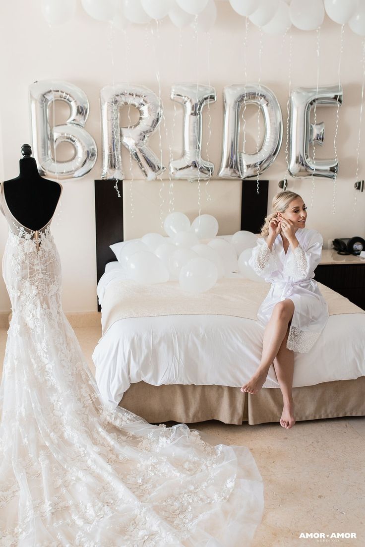 a woman sitting on a bed next to a wedding dress and balloon sign that says bride