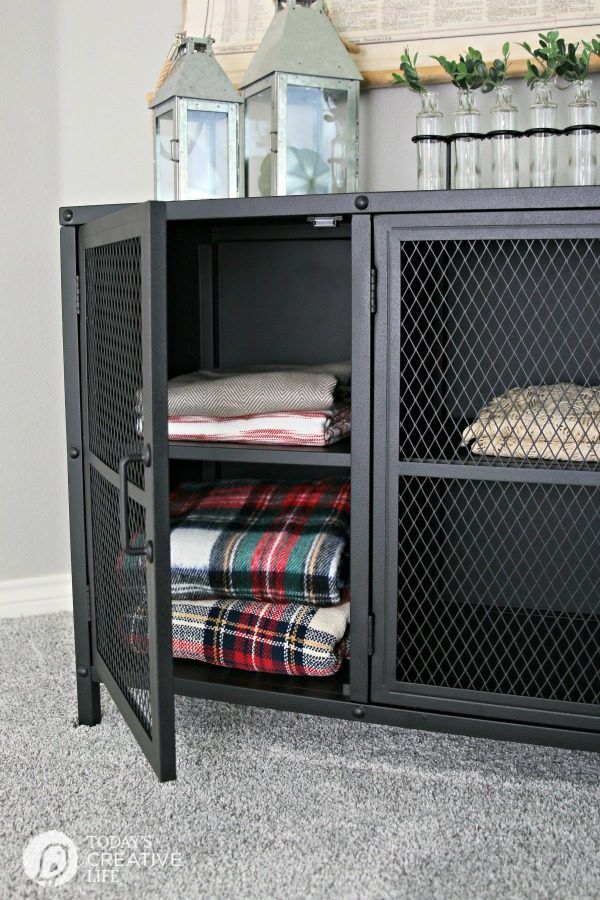 a black cabinet with some folded blankets in it and two lanterns on the wall behind it