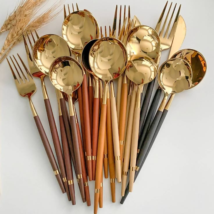 a bunch of gold colored spoons and forks on a white surface with wheat in the background