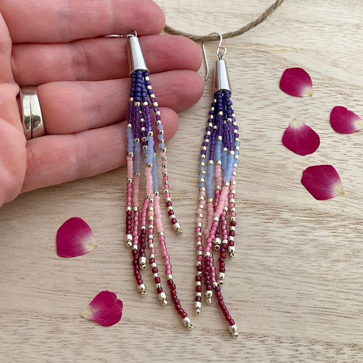 a pair of pink, blue and white beaded earrings on a wooden table with rose petals