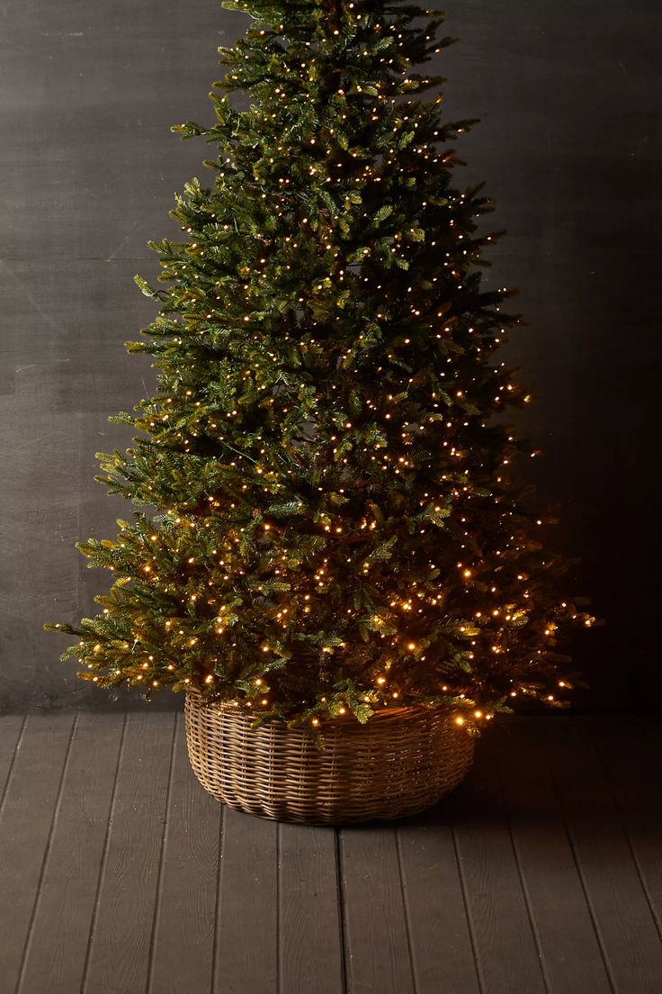 a small christmas tree in a wicker basket on a wooden floor next to a wall