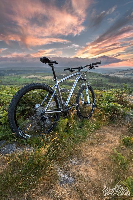 a mountain bike sitting on top of a grass covered hillside under a colorful sky with clouds