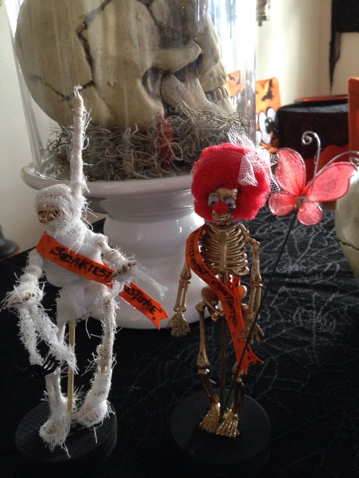 two skeleton figurines sitting on top of a table next to a vase filled with flowers