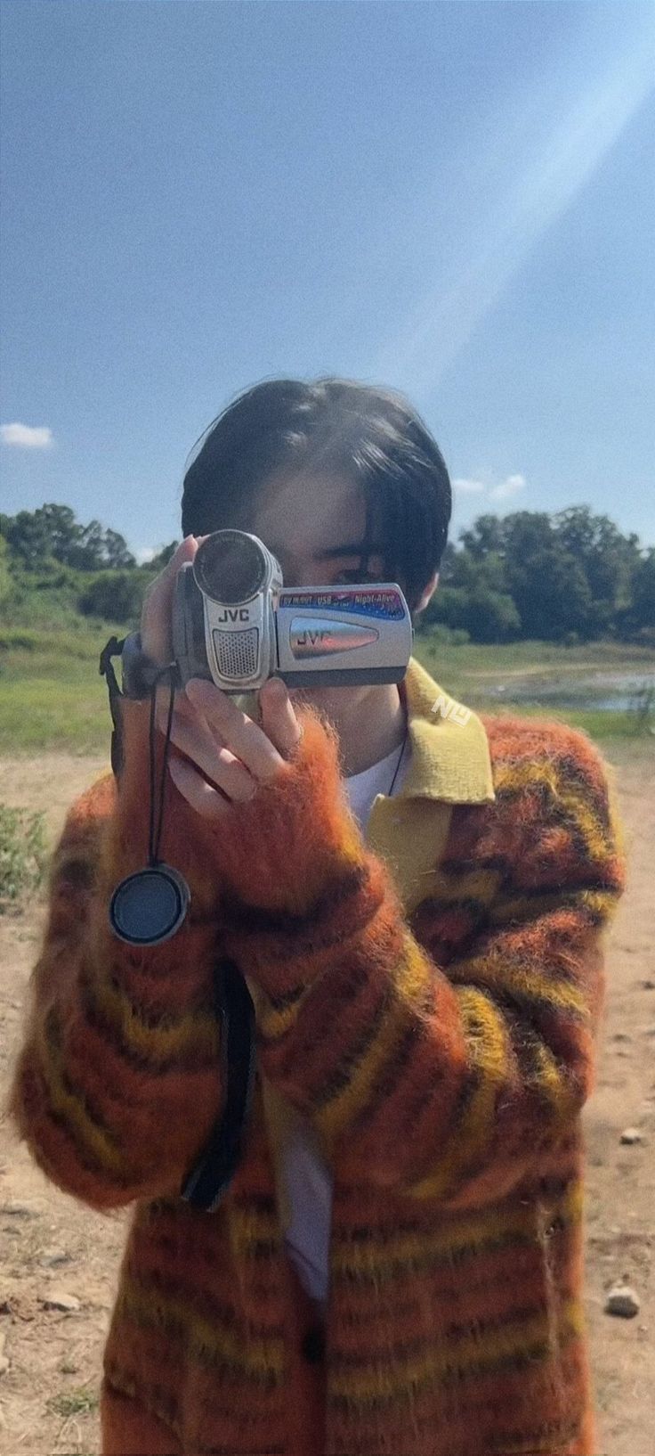 a woman taking a photo with her cell phone while wearing a fuzzy sweater and holding a camera up to her face