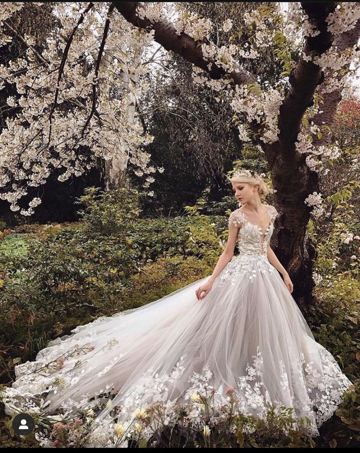 a woman in a wedding dress standing next to a tree with white flowers on it