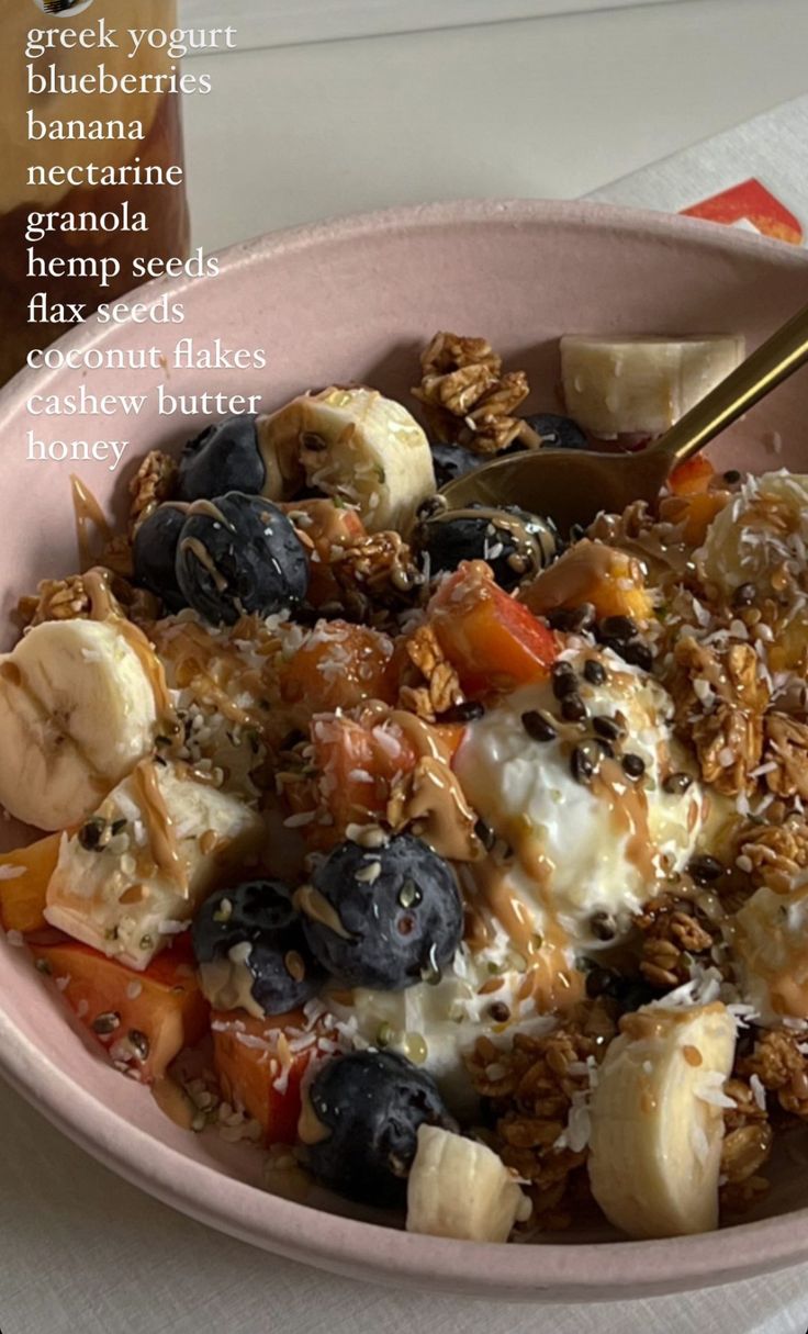 a pink bowl filled with granola, fruit and yogurt on top of a table