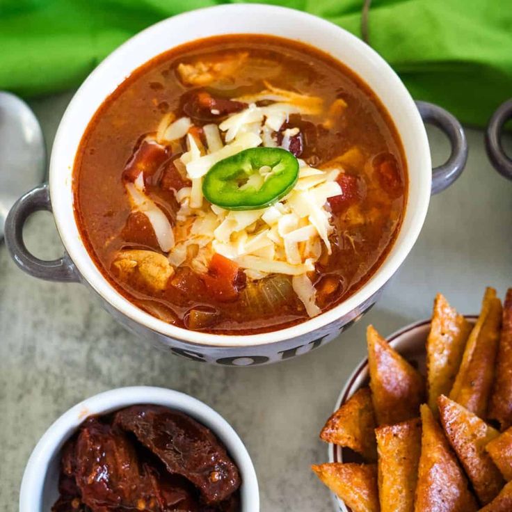 two bowls of chili and cheese soup next to some pita chips on a table