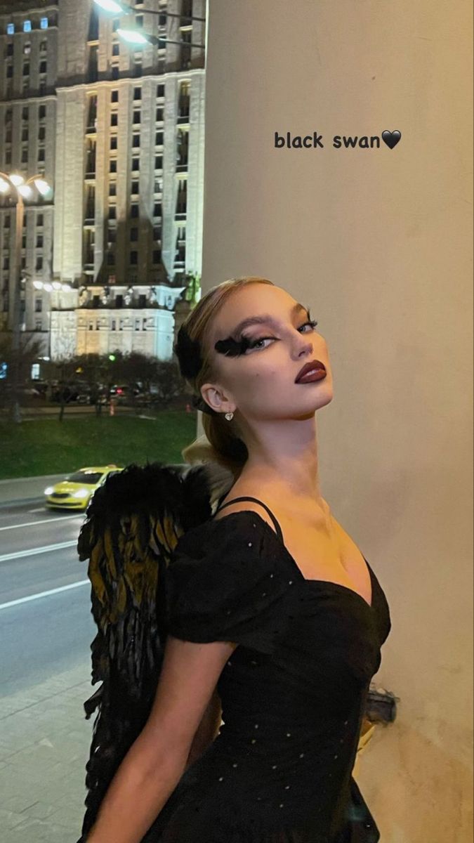 a woman in a black dress standing next to a tall building at night with her eyes closed