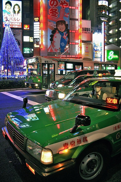 taxi cabs are parked on the side of the road in front of brightly lit buildings