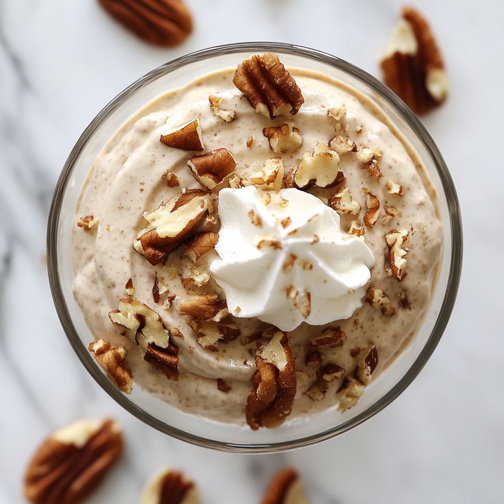 a dessert in a glass topped with whipped cream and pecans