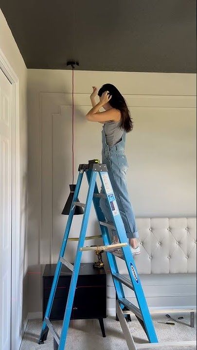 a woman is standing on a ladder and painting the walls