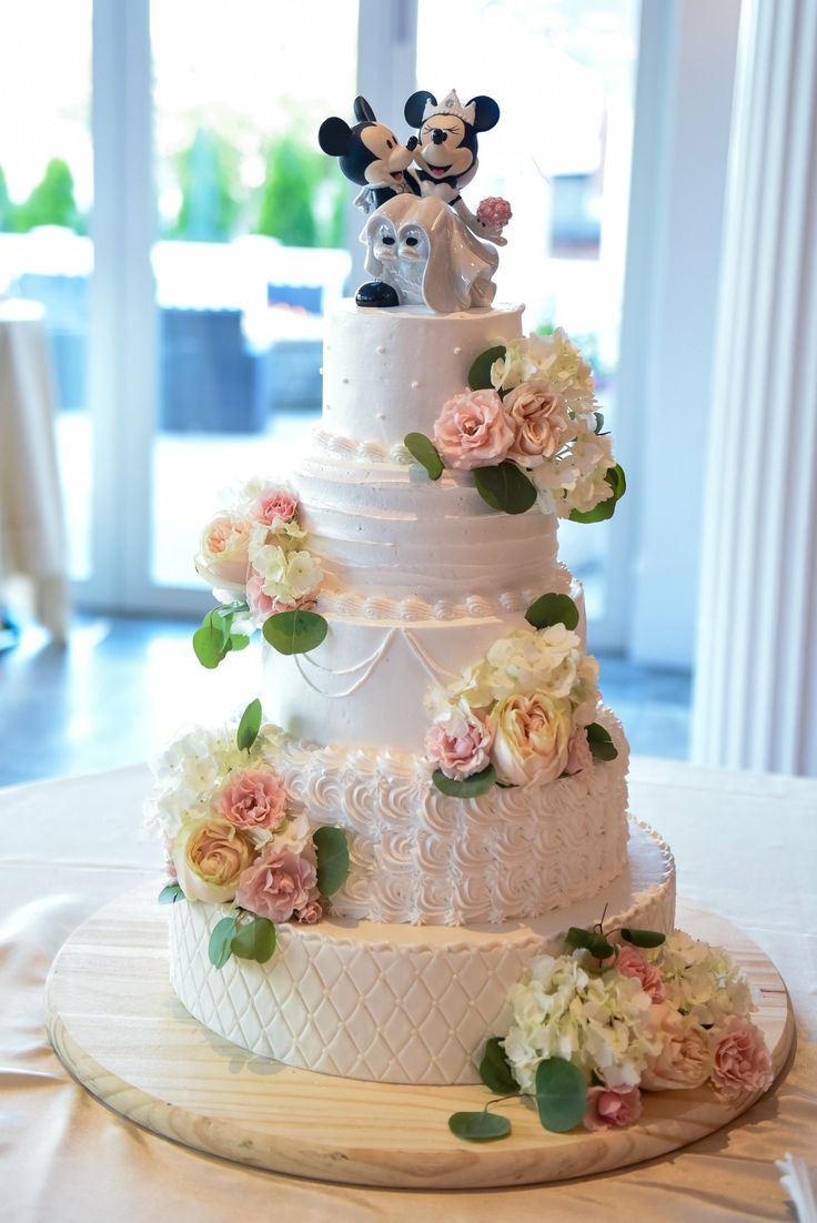 a three tiered wedding cake with flowers and mickey mouse figurines on top