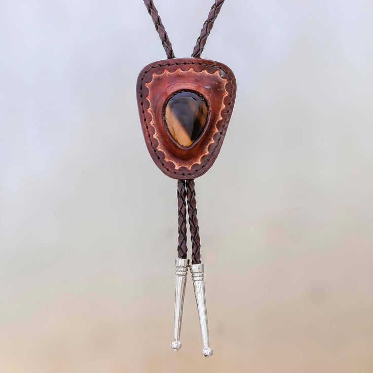 Crafted by hand the leather pendant of this bolo tie from Thailand is centered by a single tiger's eye gemstone. Chaloemphon presents this tie circling the neck with adjustable braided leather cord. Sterling silver plated brass accentuates the ends of the cord. Luxury Bohemian Lariat Bolo Ties, Leather Bolo Tie, Western Lariat Jewelry For Festival, Western Black Leather Jewelry, Western Style Black Leather Jewelry, Black Leather Western Jewelry, Brown Concho Jewelry For Rodeo, Rustic Concho Jewelry For Rodeo, Western Lariat Jewelry As Gift