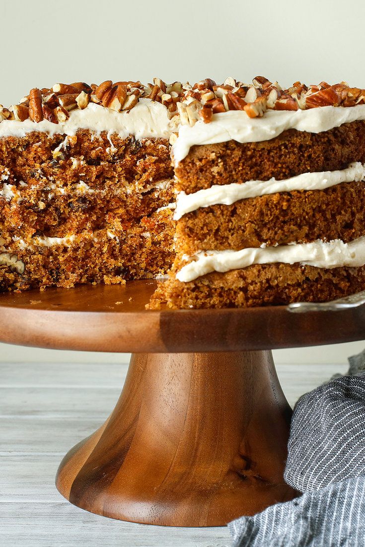 a large carrot cake with white frosting and nuts on top is sitting on a wooden platter