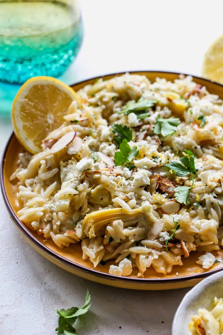 a plate full of pasta with lemon wedges and parsley on the side,