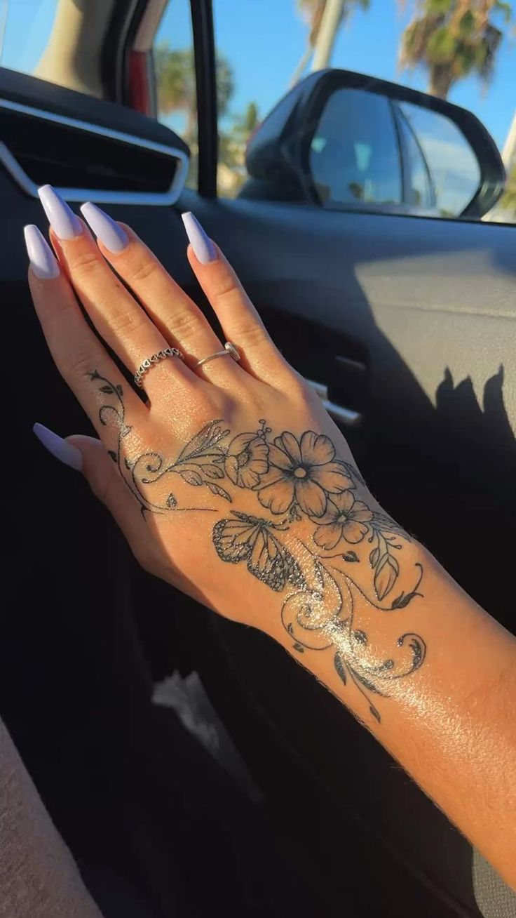 a woman's hand with flowers on her left wrist and tattoos on her right arm