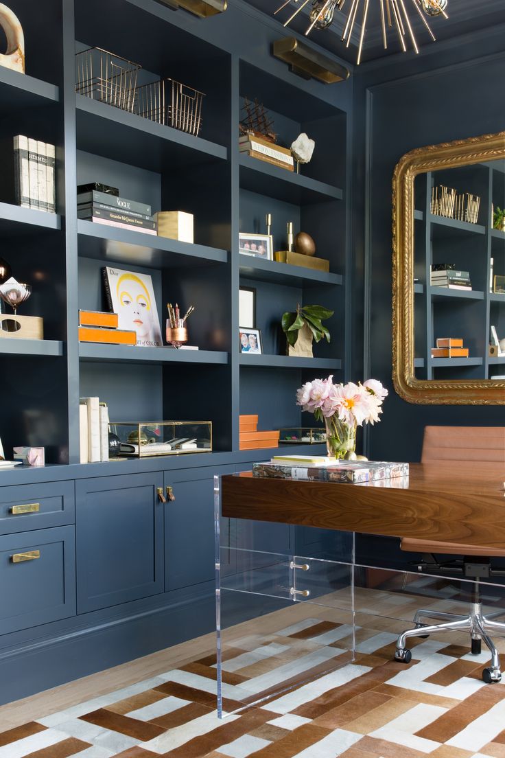 an office with blue bookcases and wooden desk in front of a gold framed mirror