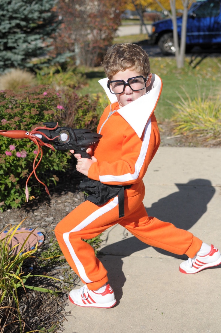 a young boy dressed in an orange and white costume with goggles, holding a baseball bat