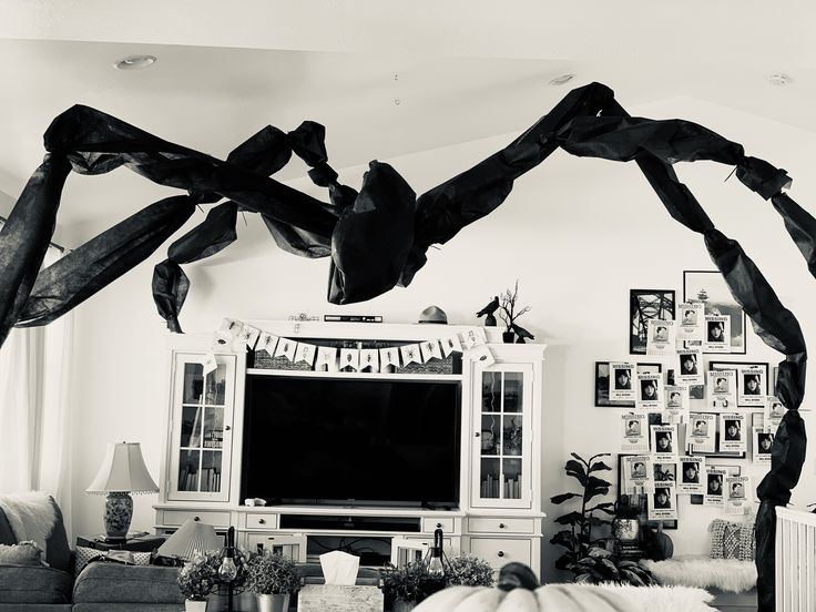 a living room filled with furniture and a large spider sculpture hanging from the ceiling in front of a flat screen tv