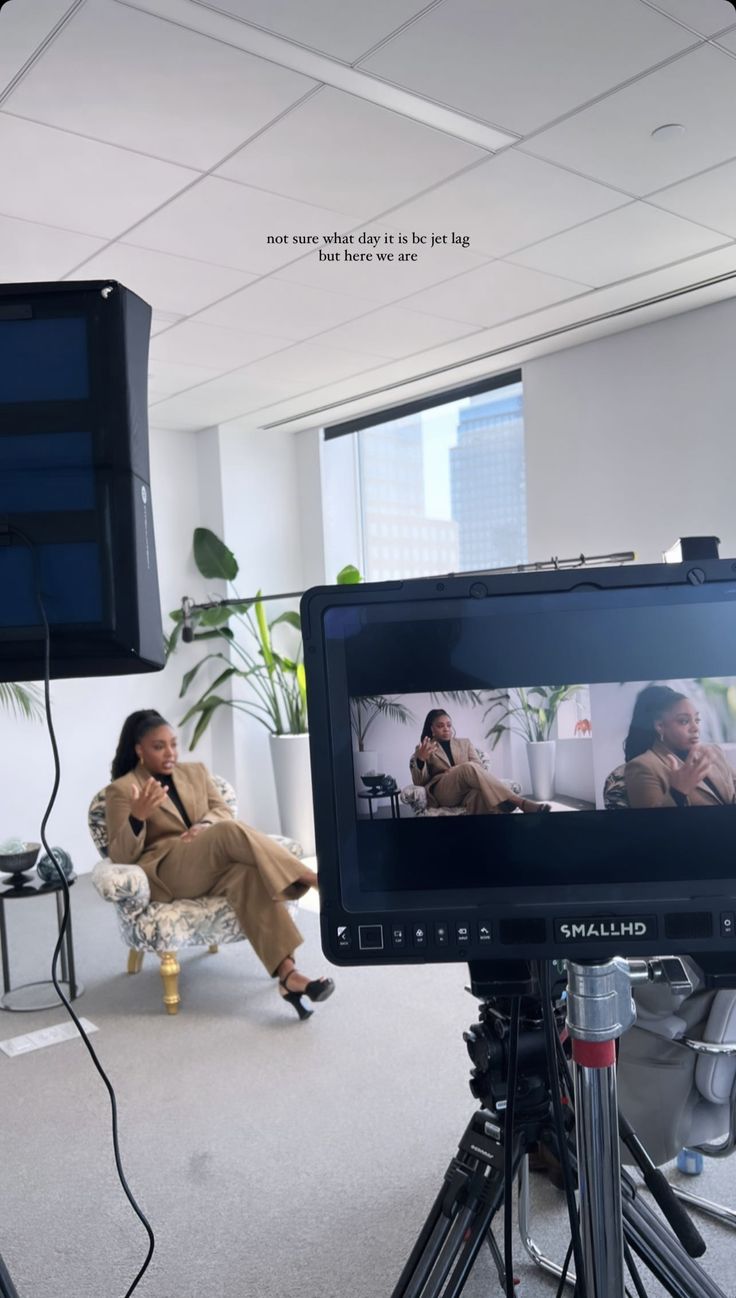 a woman sitting on a chair in front of a television screen with another person talking on the phone