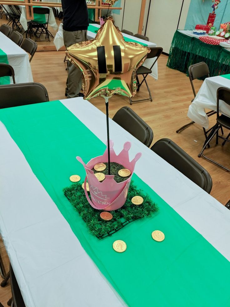 a table topped with a pink cake covered in green grass and gold foil balloons on top of it