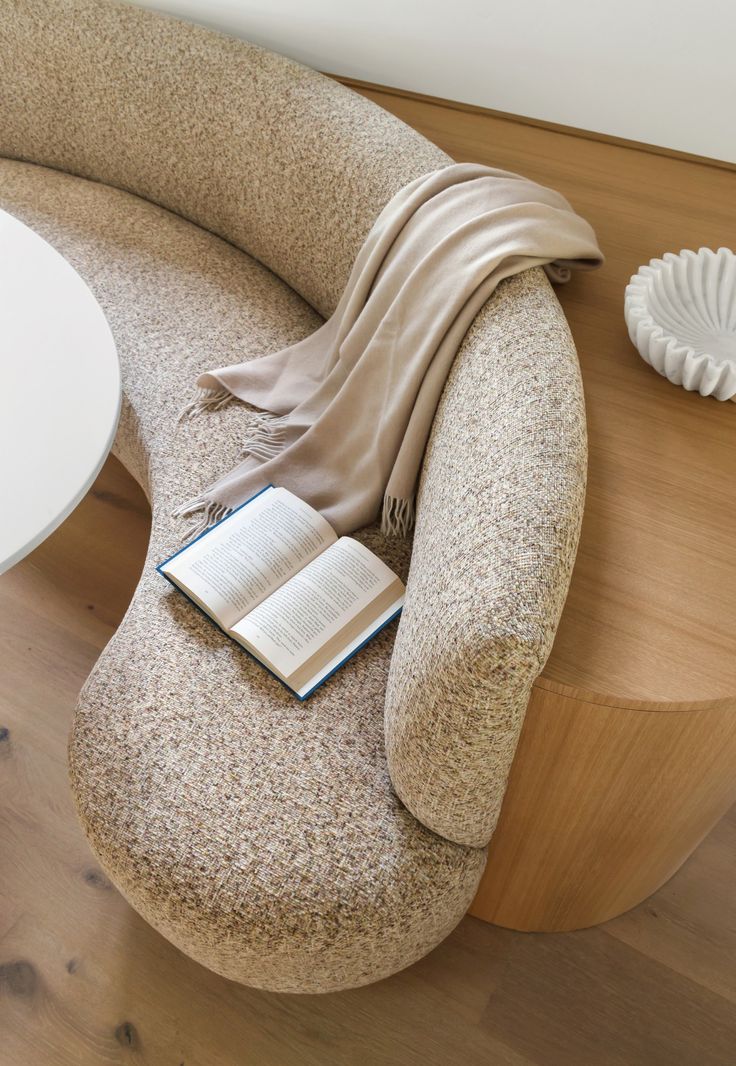 an open book sitting on top of a chair next to a white vase and table