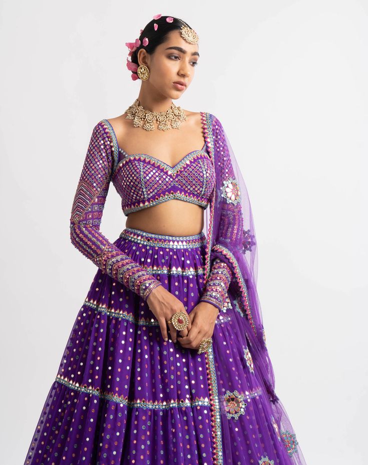 Editor's Note Intricately Hand Embroidered Multi Color Sweetheart Blouse With Multi Tier Hand Embroidered Lehenga And A Beautiful Mirror Work Dupatta. Fabric: Lehenga - Georgette Dupatta - Net Blouse - Georgette Lining - Silk Blend Color: Purple Care: Dry Clean Only About the Designer Vvani by Vani Vats- an Indian ethnic women’s wear label. It is a depiction of the royal and intricate handcrafted embroideries in unconventional designs. Designer Multicolor Pre-draped Saree With Gota Work, Designer Purple Choli With Gota Work, Purple Pre-draped Saree With Mirror Work For Navratri, Navratri Purple Pre-draped Saree With Mirror Work, Party Choli With Multicolor Embroidery And Mirror Work, Purple Anarkali Pre-draped Saree With Mirror Work, Designer Multicolor Embroidered Lehenga With Gota Work, Purple Sequined Traditional Wear For Diwali, Purple Sequins Sets For Navratri