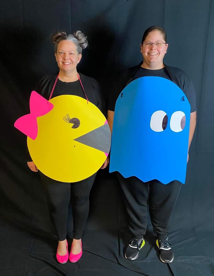 two people dressed up as pacman and chickbob holding paper cutouts in front of a black background