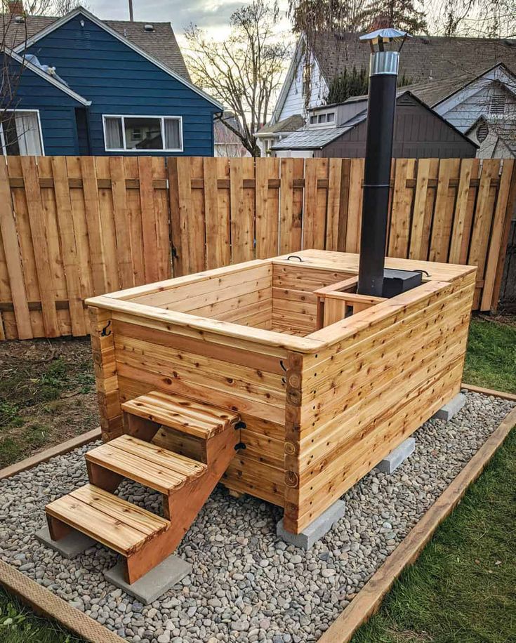 a wooden hot tub sitting on top of a gravel covered ground next to a fence